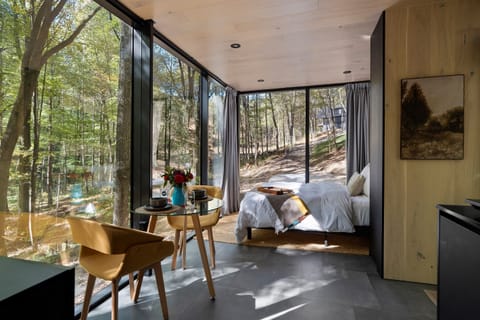 Queen bed and dining area at Thoreau — floor-to-ceiling glass on three sides, forest views from every angle