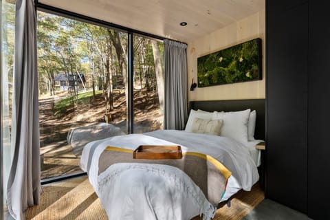 Queen bed facing floor-to-ceiling glass at Thoreau — wake up to unobstructed forest views, crisp linens, blackout curtains for nighttime privacy