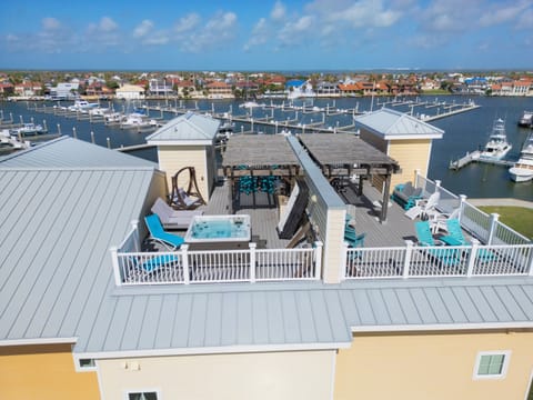 Coastal property with rooftop deck featuring hot tub, overlooking a marina and residential waterfront community.