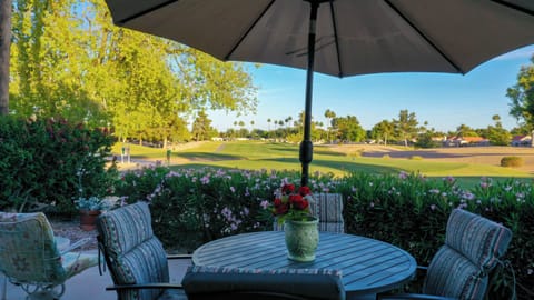 Back patio with view of golf course. Lounge chairs, table, and umbrella.