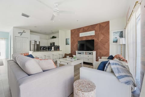 Spacious open-concept living area with coastal charm and designer touches. Relax on plush seating and enjoy the stunning wood accent wall and large TV.
