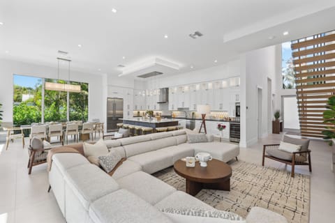 Bright & Modern Delray Beach Retreat – Spacious open-concept living with a designer kitchen, large island, and floor-to-ceiling windows showcasing lush tropical views.