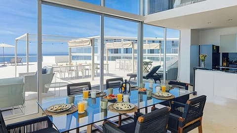 Dining table set beside glass walls, perfect for meals w/ sweeping water views