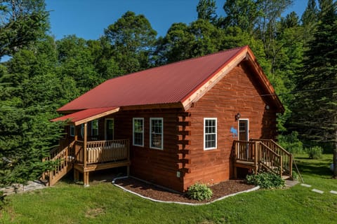 - Rustic cabin exterior with red roof design   - Surrounded by greenery and mountain backdrop   - Inviting entryways welcome you into nature stay