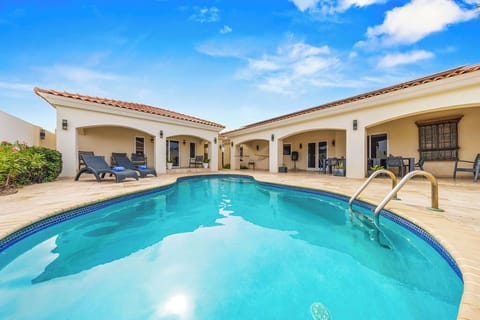 A stunning Mediterranean-style villa surrounds an inviting private pool with sparkling blue water, offering an elegant outdoor retreat under the warm sun and clear sky.