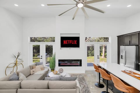 Modern living room with a wall-mounted TV and electric fireplace overlooking the backyard.