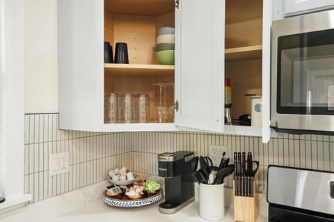 This kitchen is ready for anything—featuring a coffee bar with Keurig and pods, wine glasses, colorful bowls, stylish tumblers, and essential utensils. Whether you're brewing a morning cup or plating a full meal, it’s all here for you.