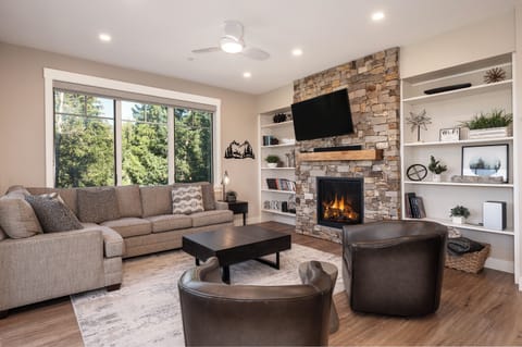 - Curl up by the stone fireplace in this bright and modern living room with forest views - Thoughtfully designed with built in shelves, plush seating, and a mounted TV - An ideal gathering space for chilly nights or laid back lounging