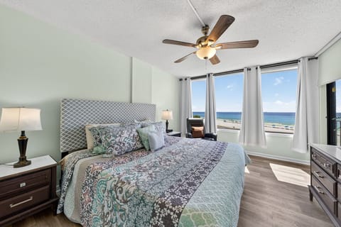 Spacious Gulf-front bedroom with panoramic views, king-size bed, modern headboard, and elegant lighting—wake up to stunning ocean scenery daily.