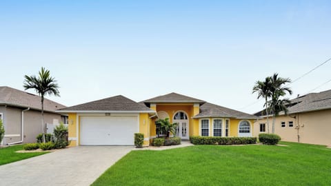 Modern vacation villa with yellow façade, well-kept front yard, palm trees, and double garage – perfect for a sunny Florida getaway.