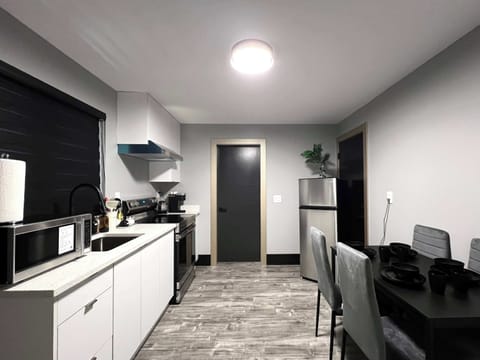 A modern kitchen with white cabinets, a microwave, stove, and a stainless steel refrigerator. The space also features a dining table with four chairs and dark wood-look floors.