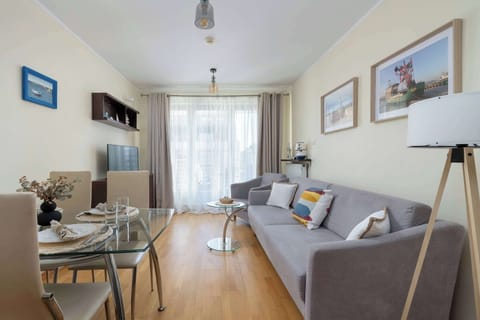 A bright living room features a gray sofa, a coffee table, and a floor lamp placed on warm wooden flooring. Large windows allow plenty of natural light to fill the space.
