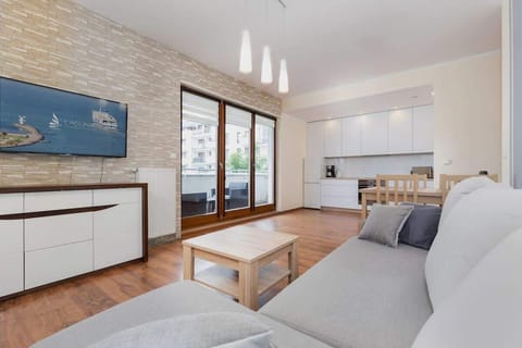 The versatile living room with kitchenette creates a functional space for spending time with loved ones. Bright interiors with a grey sofa, large TV and white kitchen furniture. 