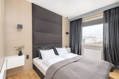 A stylish bedroom with a king-size bed, elegant dark headboard, and large windows allowing natural light to flood in. Cozy curtains and neutral tones create a relaxing atmosphere.