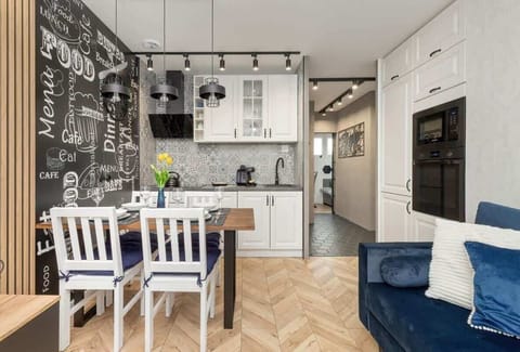 A contemporary kitchen with white cabinetry, patterned backsplash, and stainless steel appliances. The open layout connects seamlessly to the living room.