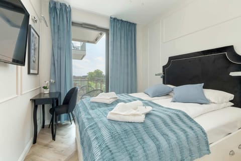 A stylish bedroom with twin beds and elegant blue bedding, complemented by modern decor and ample natural light. A large window with blackout curtains ensures privacy and restful sleep.
