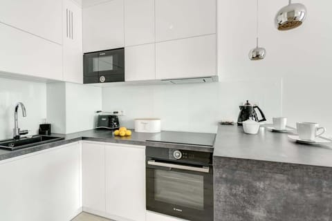 A modern, minimalist kitchen with sleek white cabinetry, a black sink, and built-in appliances, complemented by metallic pendant lights and a dark countertop.