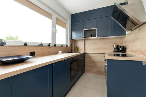A modern kitchen with navy blue cabinets, wooden countertops, and built-in appliances.