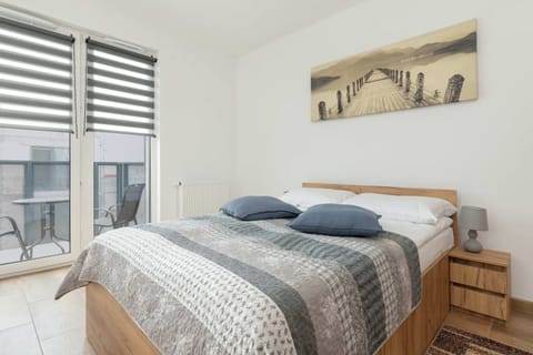 A neatly made bed with patterned bedding dominates the frame, with a small shelf and decorative items visible in the background.