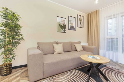 A cozy living room featuring a large beige sofa, a plant in the corner, and natural light from the window.