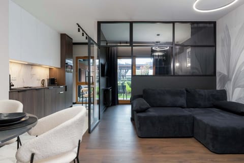 A modern apartment interior where the living area with a black sofa was separated from the bedroom by a glass wall.