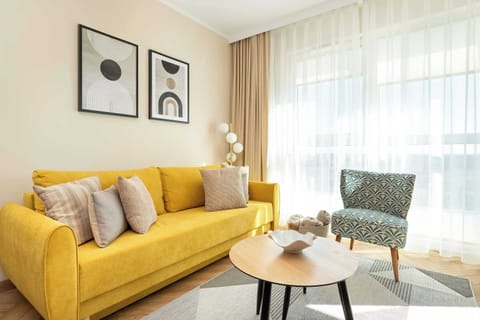 A cozy living room featuring a mustard yellow sofa, modern wall art, and a small round coffee table set on a wooden floor.