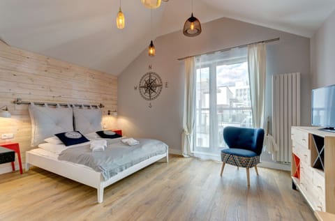 A cozy studio with a nautical theme, featuring a bed, sitting area, and large windows letting in natural light.