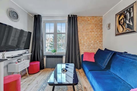 The spacious and stylish living room exudes modern design, combining functionality with aesthetics. A comfortable, fold-out sofa in a deep hue serves as the centerpiece, inviting relaxation. The exposed brick wall adds an industrial charm.