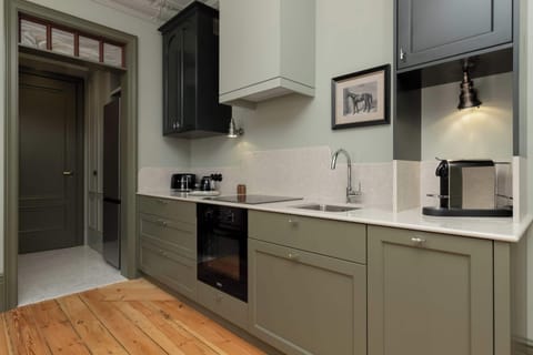 A modern kitchen with muted green cabinetry, built-in appliances, and a wooden floor.