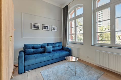 A bright and cozy studio with a blue sofa, arched windows, and framed artwork adding a decorative touch.