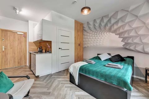 Dynamic geometric mural on the wall, complemented by sleek, minimalist furnishings and a warm wood-toned kitchen, creating a cozy and chic atmosphere perfect for a relaxing stay.