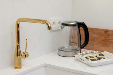 On the kitchen worktop, next to the electric kettle, there is a gold sink mixer, adding to the elegance of the modern setting.