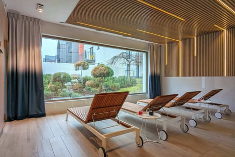 A bright, airy relaxation room with a large window onto the garden, furnished with wooden loungers and lit by a lamella ceiling, creates a peaceful atmosphere.