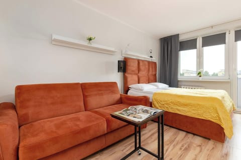 A cozy studio layout with a rust-orange sofa, yellow bedding, and wooden furnishings, blending the sleeping and living areas seamlessly.