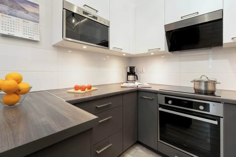 A modern kitchen with dark and white cabinets, a built-in oven, and a stovetop. Bright lighting emphasizes the clean, sleek design.