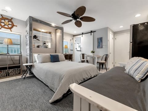 Sink into comfortable beds dressed in soft linens, cooled by a gentle ceiling fan. Your charming nautical-themed space features a cozy dining nook and barn door details that blend coastal style with modern comfort.