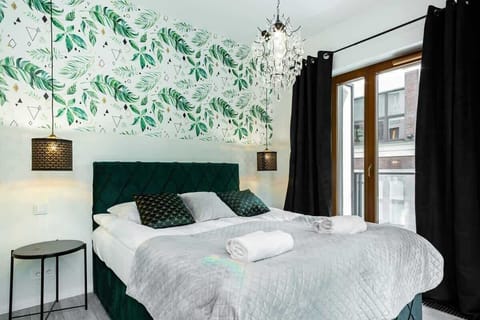 A modern bedroom with a comfortable bed, decorative green pillows, and a nature-inspired wallpaper, providing a relaxing and fresh ambiance.