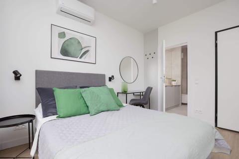 A cozy bedroom with a double bed dressed in white and green, featuring framed artwork and natural lighting.