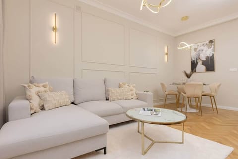 A stylish living room with a white corner sofa, decorative pillows, a glass coffee table, and elegant wall paneling.

