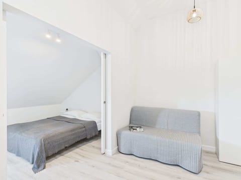 A bright attic living room with a gray sofa bed and sloped ceiling. The simple furnishings enhance the cozy and calm ambiance.