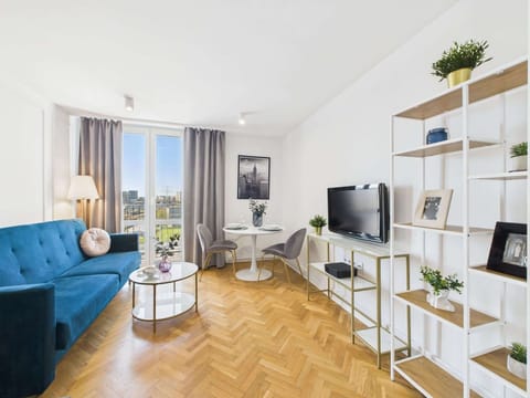 A bright living room with a large blue corner sofa, white coffee table, and open shelving filled with greenery and decor.