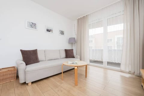 A bright living room with a beige sofa, a wooden coffee table, and sheer curtains allowing natural light to flood the space.