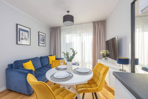 A bright living room featuring a comfortable blue sofa with yellow pillows, a small coffee table, and a dining area in the background.