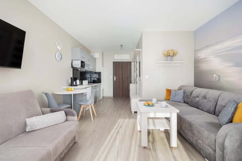 Living room from another angle, showcasing the same gray sectional sofa and white coffee table, with a glimpse of a television in the distance.