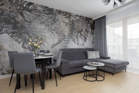 A modern living and dining area with a grey sofa set, round coffee table, and a striking botanical wall mural.