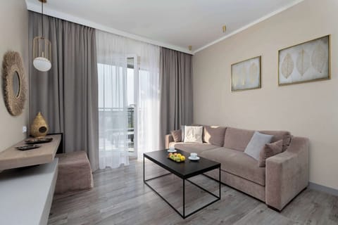 A cozy living room space with a sofa, coffee table, and TV. The large window brings in natural light, creating a warm and inviting atmosphere.