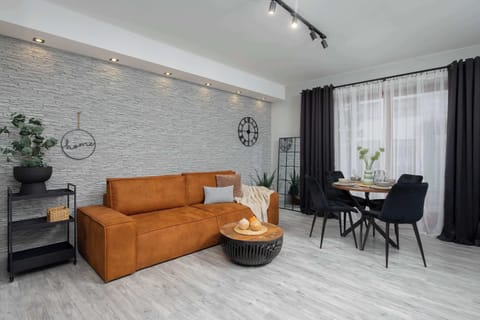 A modern living room with an orange sofa, a round coffee table, and a textured gray accent wall. The room has a contemporary design with stylish lighting.