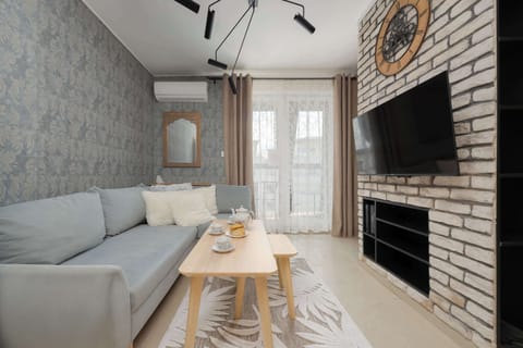 A modern, open-plan living room with a dining table, stylish wallpaper, and large windows that let in natural light.