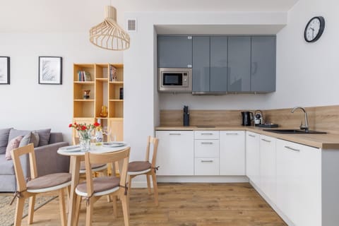The modern kitchenette design harmoniously matches the entire interior. White and gray cabinets hold all the necessary dishes, and the wooden countertop is perfect for preparing home-cooked meals.
