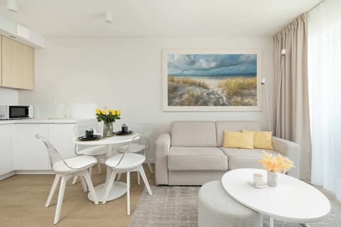 A bright living room with a comfortable sofa, coffee table, and dining space. Large windows let in plenty of natural light.